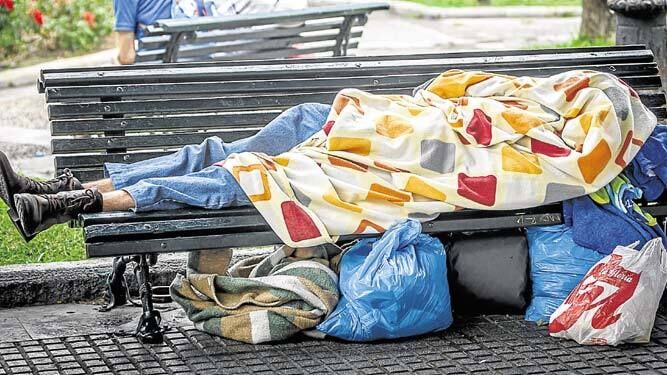 Una persona sin hogar durmiendo en un banco de la ciudad.